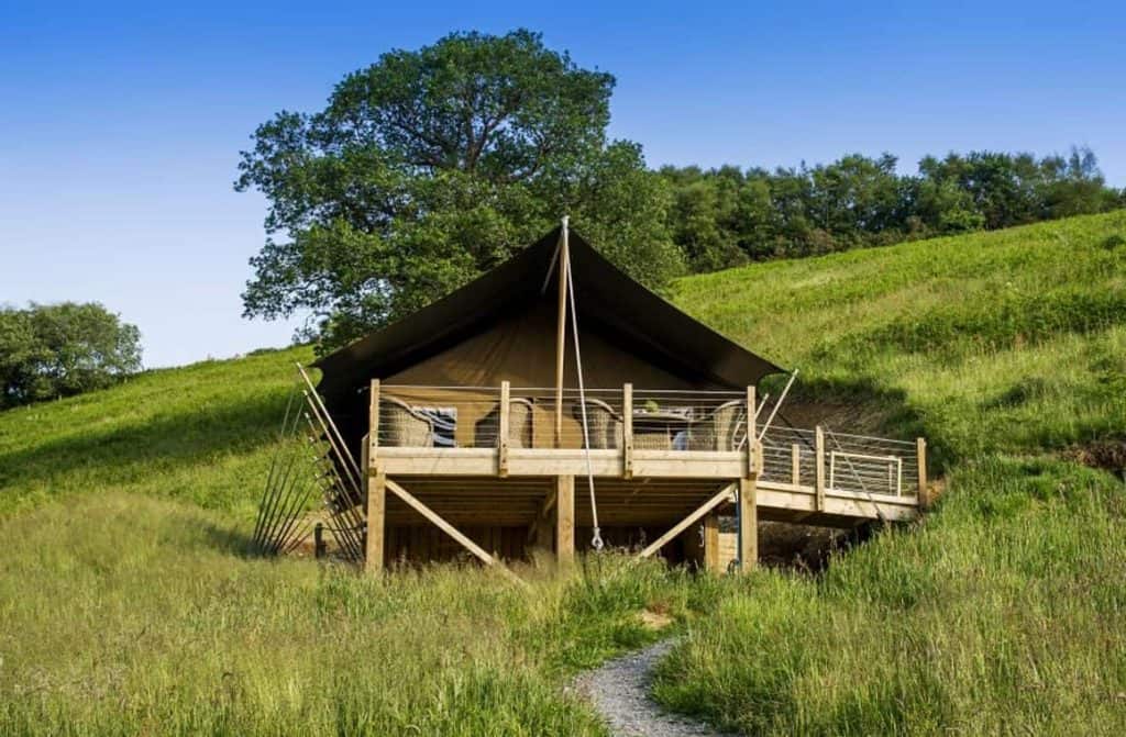 Elegant safari tent at Longlands glamping site, with outdoor deck and seating area, situated among the scenic hills of Exmoor near the coastline.