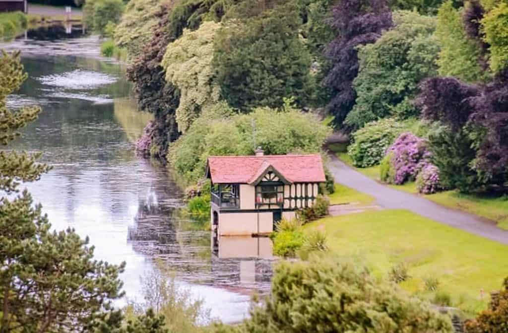 A picturesque boathouse nestled by a tranquil lake, surrounded by lush greenery and vibrant flowers.
