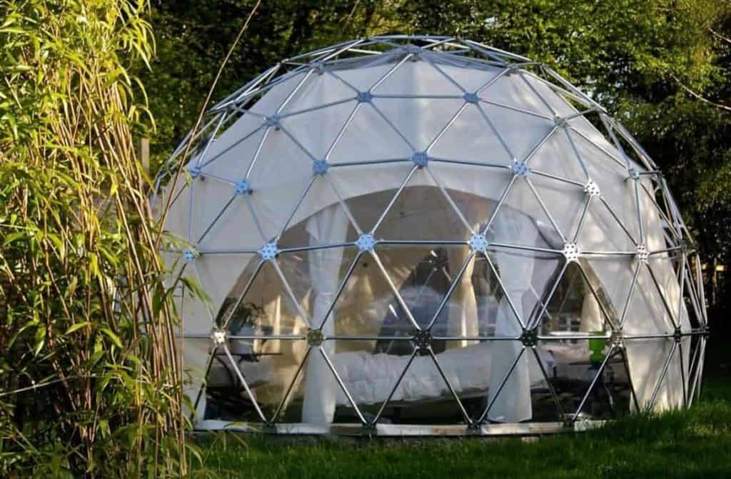10 Best U.K. Glamping Sites: A spherical double dome tent surrounded by trees and plants, featuring a transparent panel for stargazing and a comfortable interior setup.