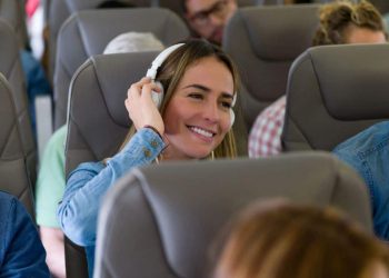 Photo of a woman enjoying music on a plane with noise-canceling headphones, smiling with opened eyes and a serene expression