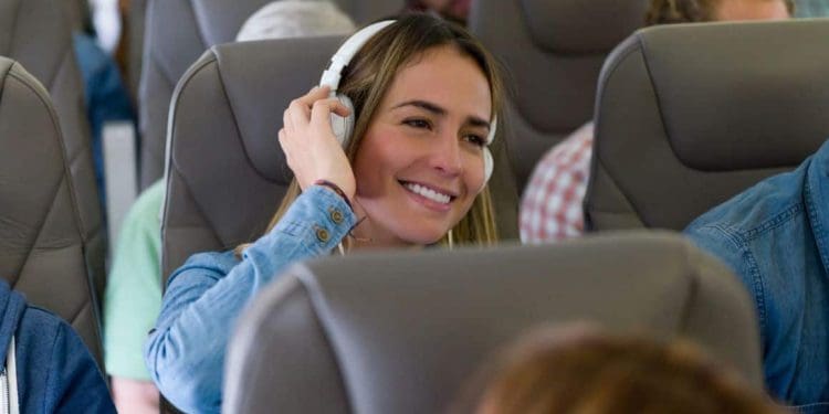 Photo of a woman enjoying music on a plane with noise-canceling headphones, smiling with opened eyes and a serene expression