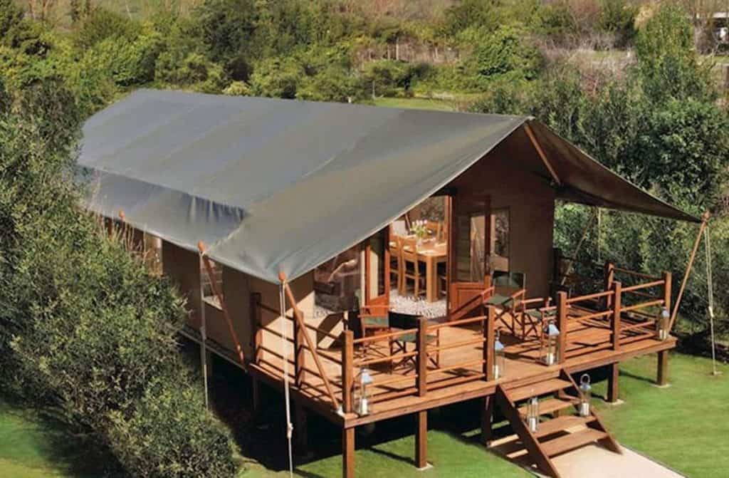 Several spacious safari tents lined up amidst lush greenery, featuring comfortable outdoor seating areas and a tranquil environment.