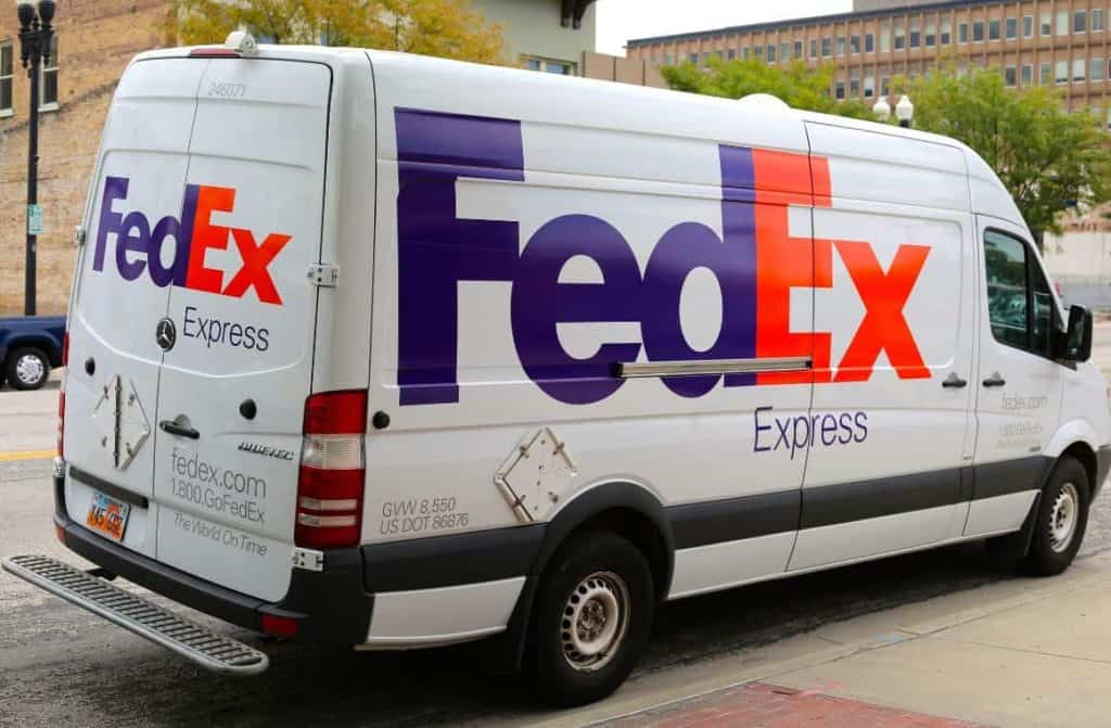 A white and purple FedEx delivery van parked on the street.
