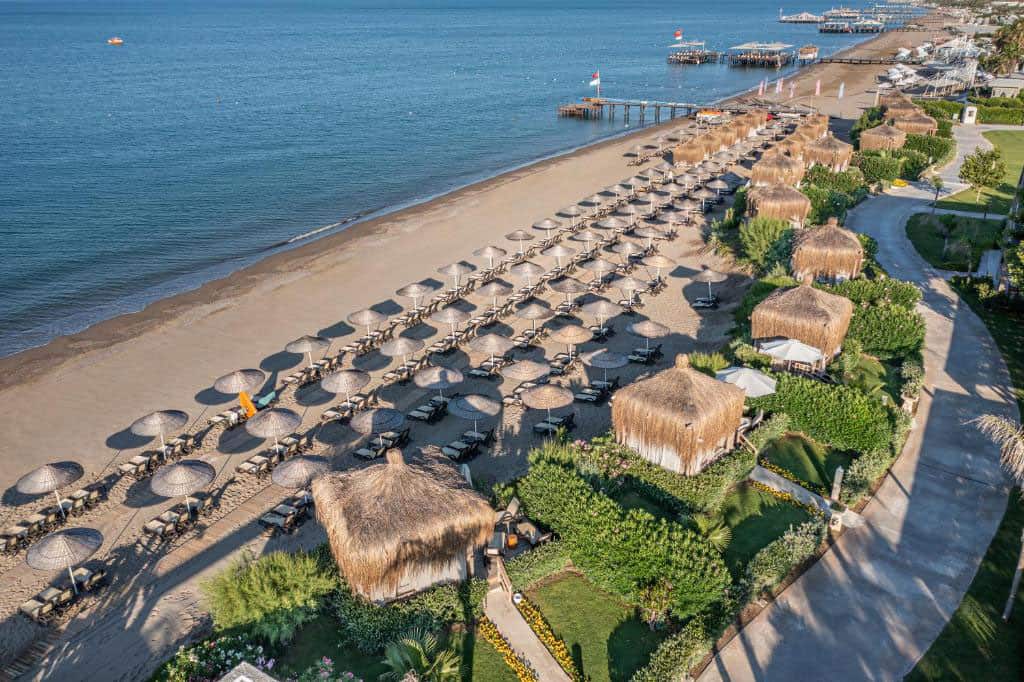 The image captures the serene beauty of Ela Excellence Belek, a luxurious resort set in the heart of Turkey's enchanting coastline. The resort is framed by a picturesque beach, with its golden sands meeting the clear, calm waters of the Mediterranean Sea.