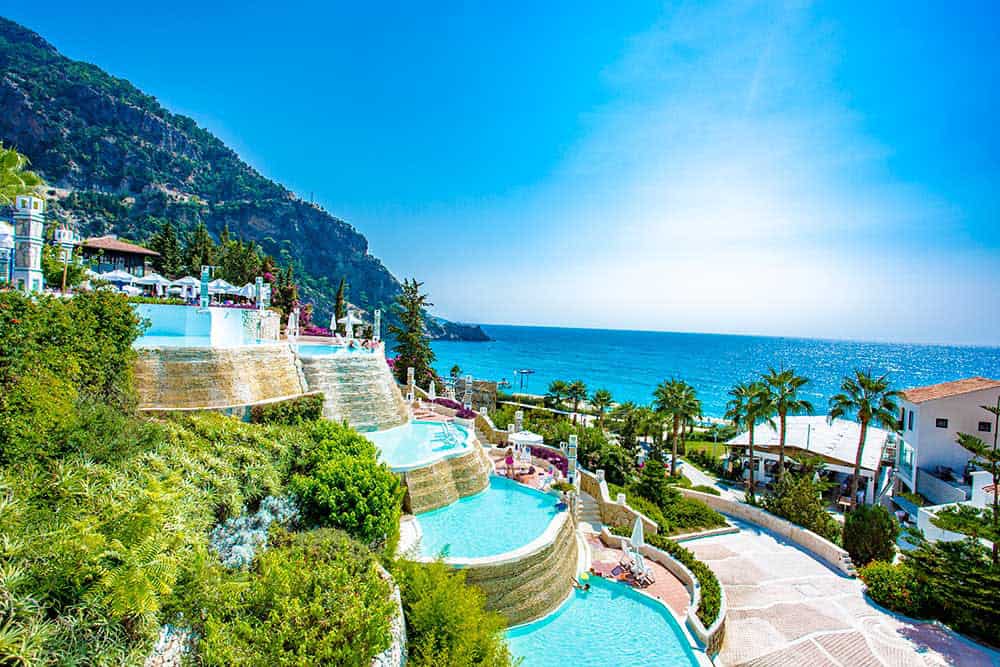 This image beautifully showcases Liberty Hotels Lykia, a luxurious coastal resort nestled along Turkey's pristine shores. The resort is pictured against a breathtaking backdrop of the deep blue sea, highlighting its idyllic beachfront location.