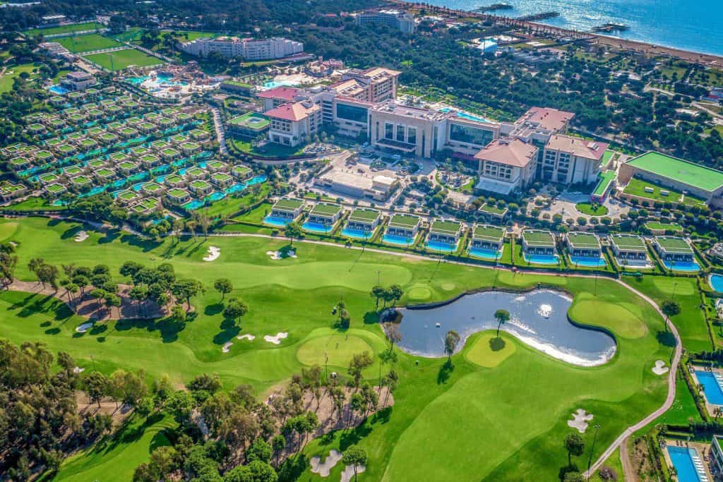 This image splendidly showcases the Regnum Carya Golf Resort, a luxurious destination for golf enthusiasts and travelers seeking refined leisure in Turkey. The resort is set against the backdrop of a world-class golf course, with beautifully manicured fairways and greens that weave through the landscape.