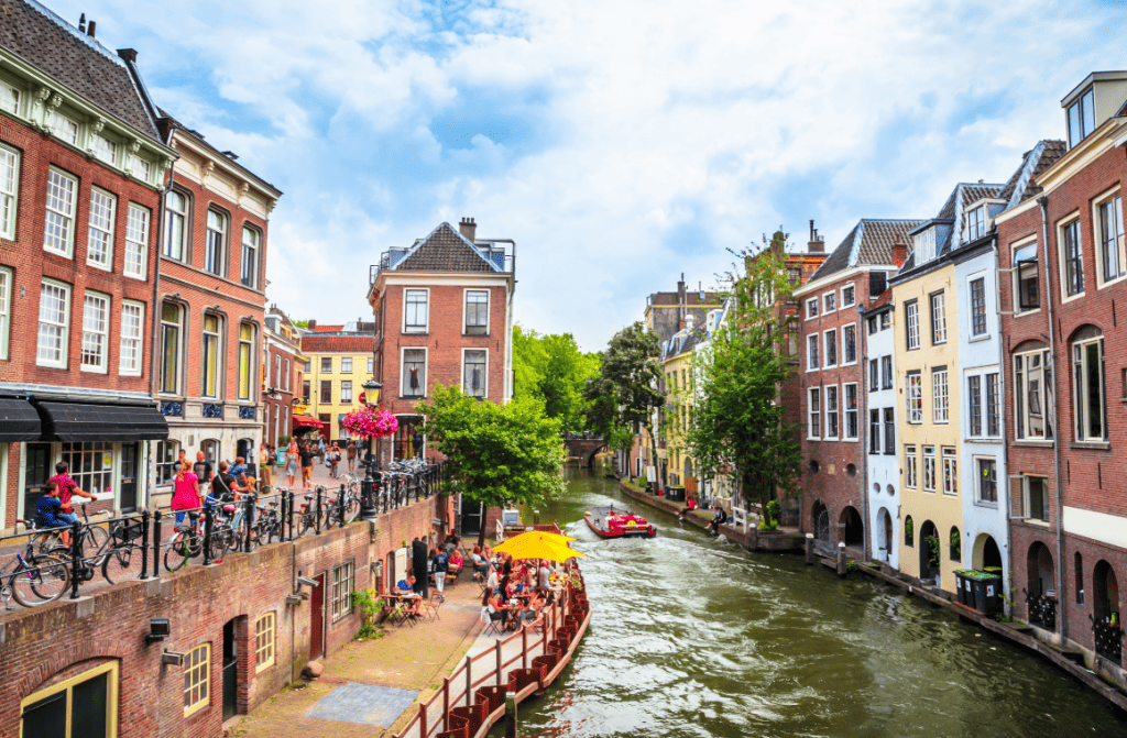 Peaceful view of Utrecht, Netherlands, featuring the Oudegracht canal with wharf cellars, boats, and historic Dutch houses, with the Dom Tower in the backdrop.