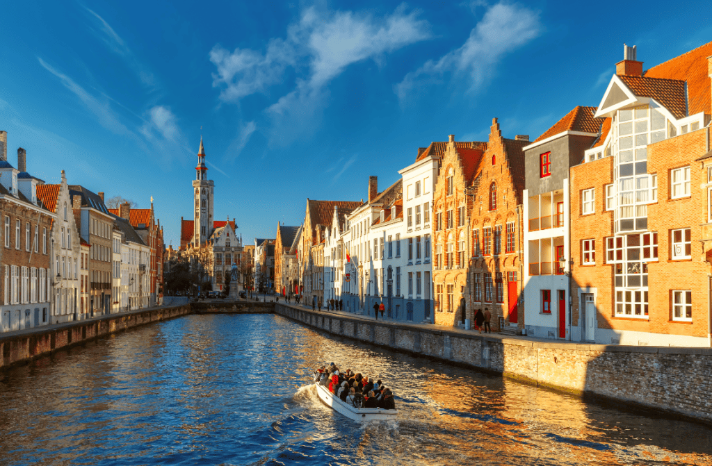 Tourists enjoying a boat tour along the canals of Bruges, Belgium, with historic buildings in the background.