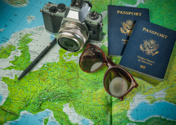 Two American passports with a European map in the background, alongside dark sunglasses and a camera, symbolizing travel preparation.